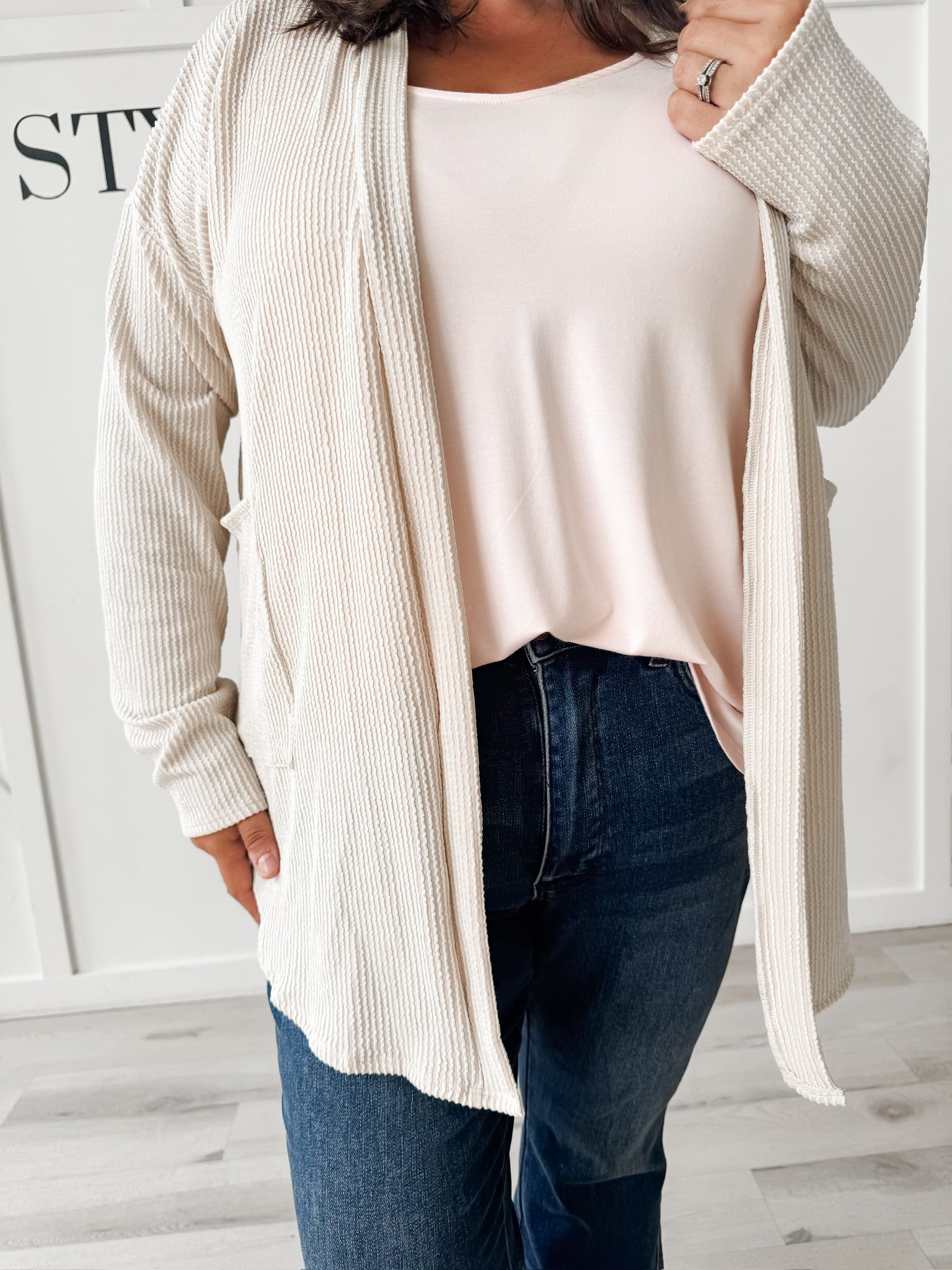 Person wearing a beige cardigan over a white top and blue jeans 