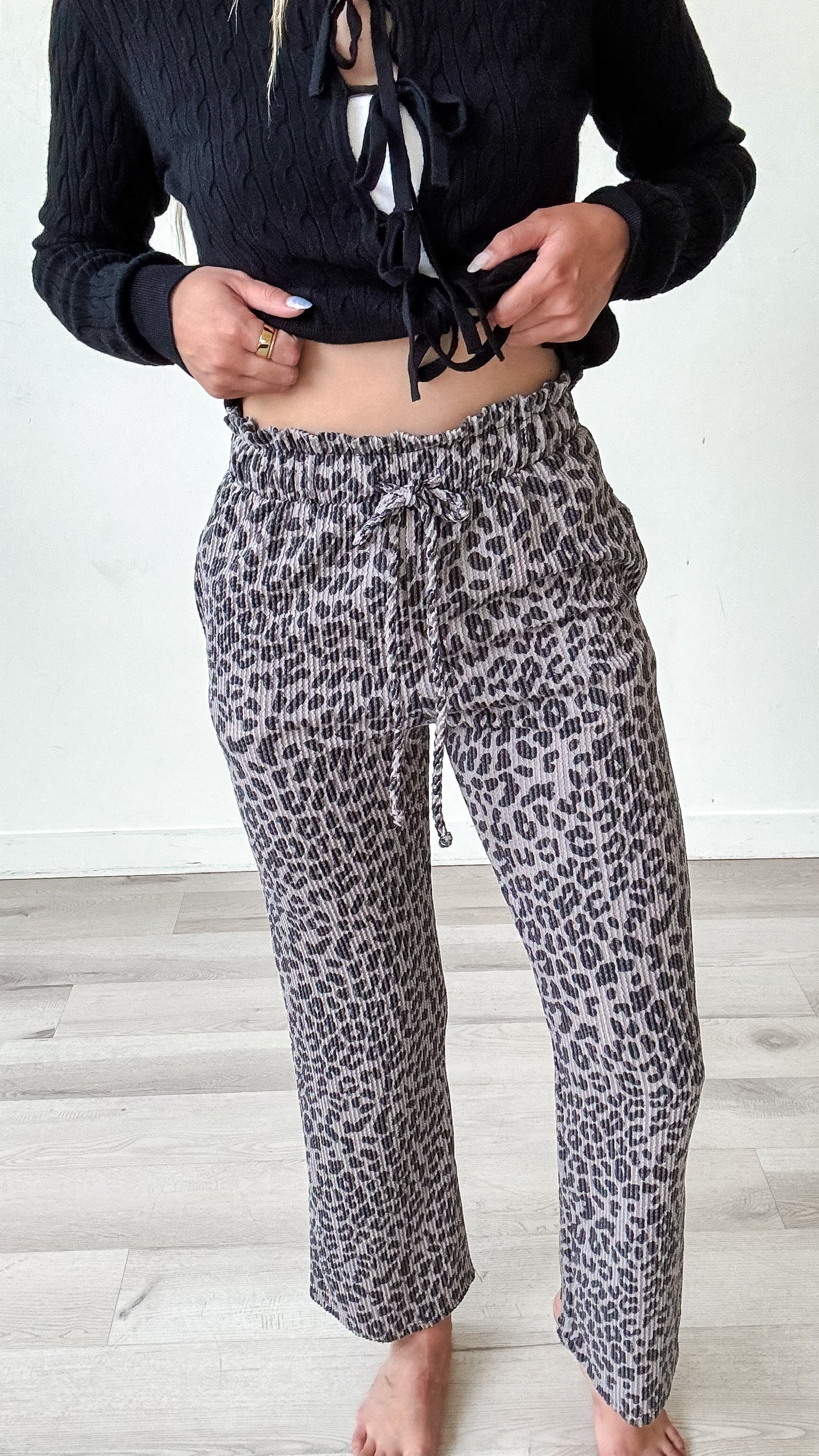 Person wearing a black cropped top and leopard print pants on a light wooden floor.
